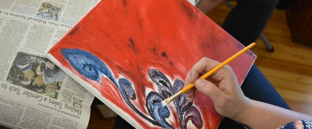 A painter covers a canvas with red paint and a blue flower.