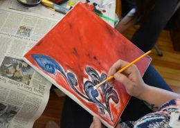 A painter covers a canvas with red paint and a blue flower.