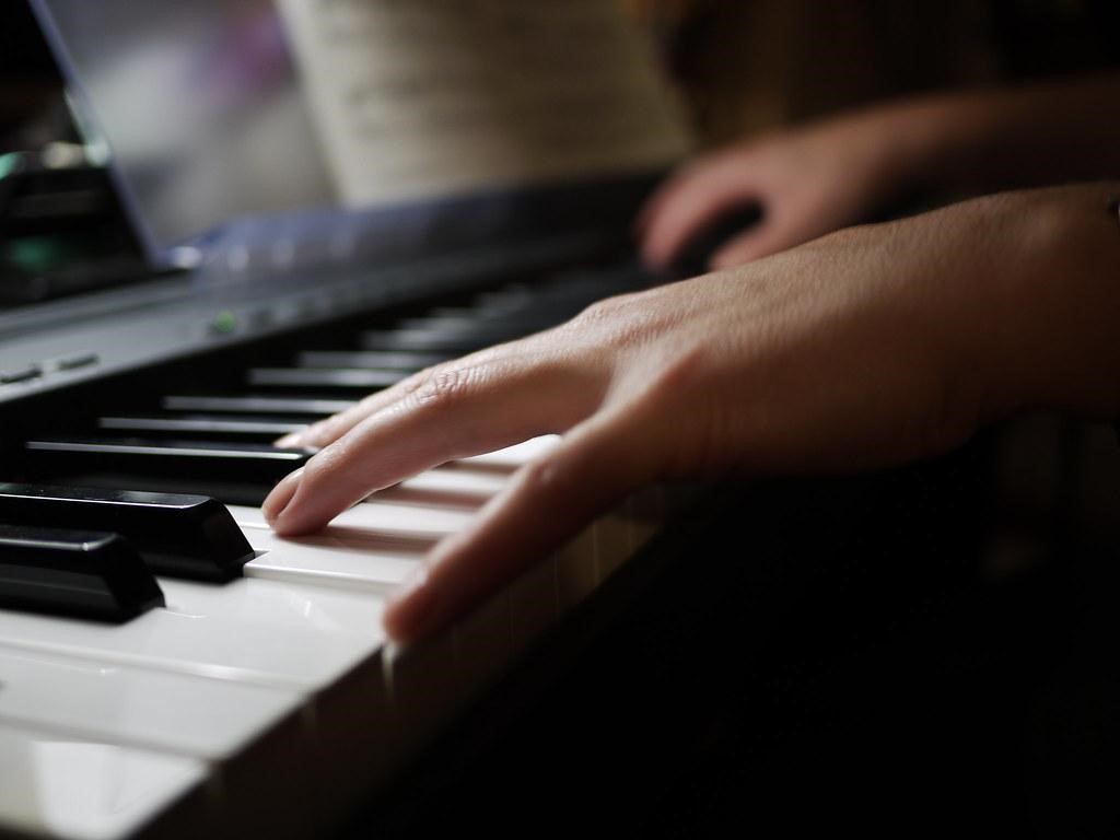 Hands rest on illuminated piano keys, surrounded by darkness. A musical instrument can be a great way to de-stress and take time for yourself.