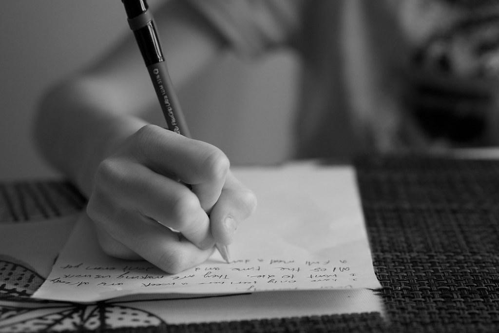 A hand holding a pen is shown writing on paper. Journaling or creative writing can be a great stress reliever.